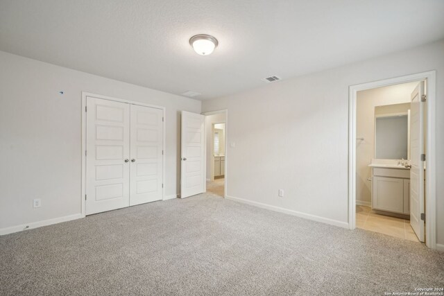 unfurnished bedroom with ensuite bathroom, a closet, and light carpet