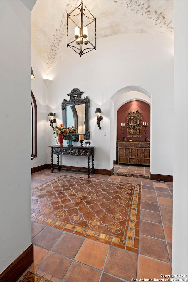 hall featuring an inviting chandelier, brick ceiling, and vaulted ceiling