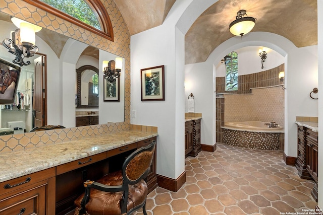 bathroom with tiled bath, plenty of natural light, vanity, and vaulted ceiling