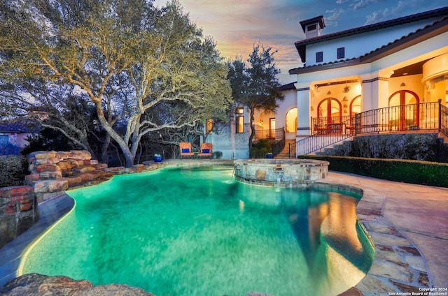 pool at dusk with an in ground hot tub