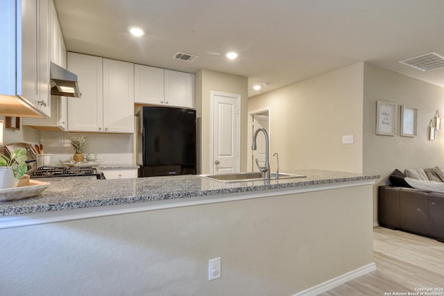 kitchen featuring white cabinetry, black fridge, light stone counters, range hood, and kitchen peninsula