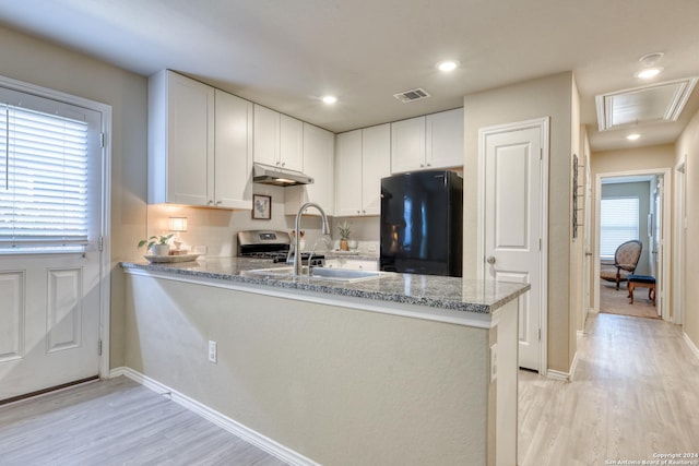 kitchen featuring black refrigerator, kitchen peninsula, and white cabinetry