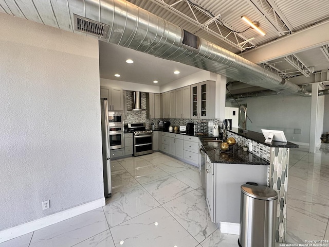 kitchen with appliances with stainless steel finishes, wall chimney range hood, dark stone countertops, tasteful backsplash, and sink