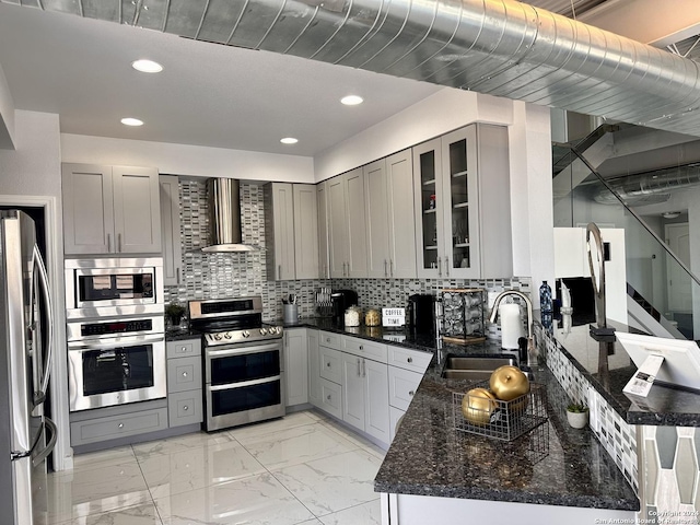 kitchen with appliances with stainless steel finishes, wall chimney exhaust hood, dark stone counters, tasteful backsplash, and sink