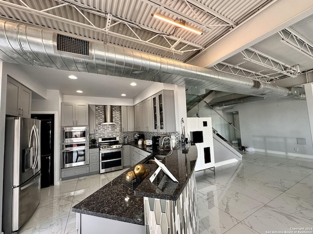 kitchen featuring wall chimney range hood, stainless steel appliances, dark stone counters, and gray cabinetry