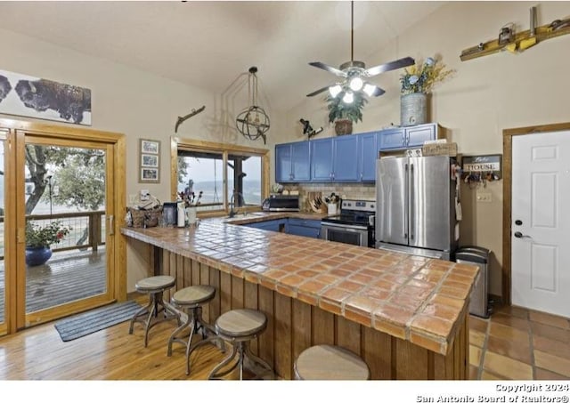 kitchen featuring light hardwood / wood-style floors, kitchen peninsula, stainless steel appliances, blue cabinets, and high vaulted ceiling