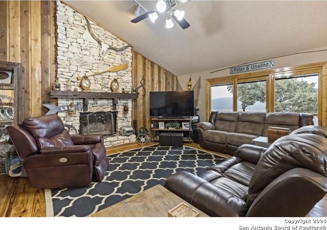 living room featuring a stone fireplace, ceiling fan, hardwood / wood-style floors, wooden walls, and high vaulted ceiling