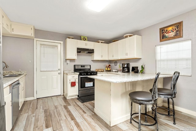 kitchen with stainless steel appliances, light stone counters, kitchen peninsula, light hardwood / wood-style floors, and a breakfast bar area