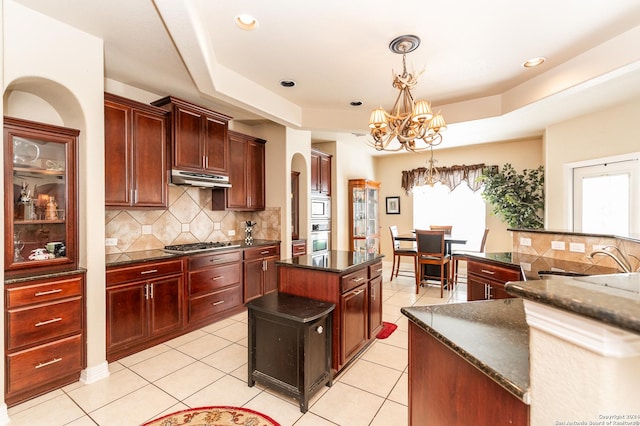 kitchen with stainless steel appliances, a raised ceiling, pendant lighting, an inviting chandelier, and a center island