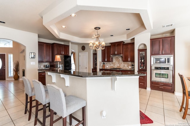 kitchen with appliances with stainless steel finishes, a center island with sink, tasteful backsplash, and light tile patterned flooring