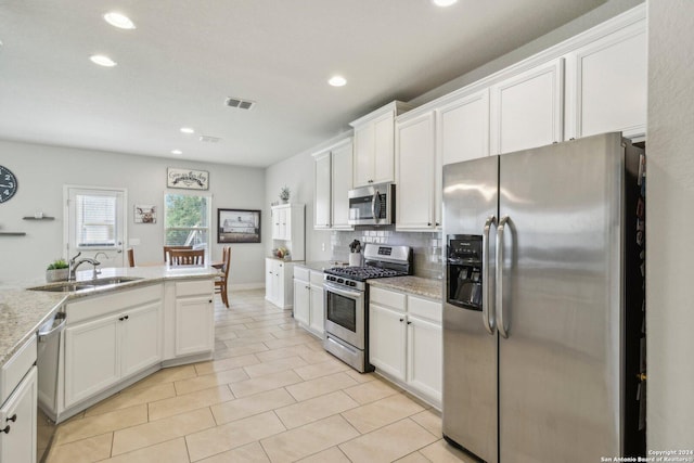 kitchen featuring decorative backsplash, light stone countertops, stainless steel appliances, sink, and white cabinets