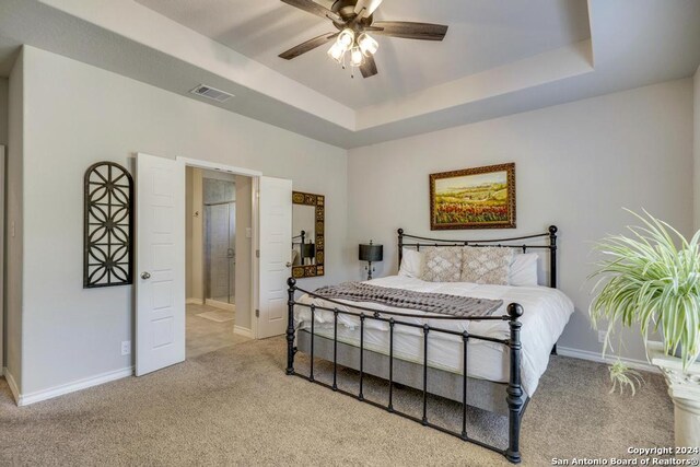 carpeted bedroom featuring ceiling fan, connected bathroom, and a tray ceiling