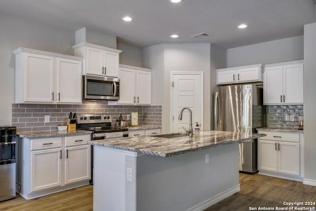 kitchen with appliances with stainless steel finishes, sink, white cabinets, light stone counters, and an island with sink