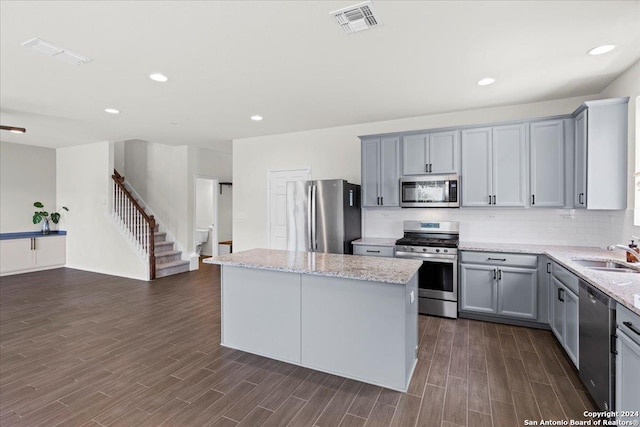 kitchen with sink, stainless steel appliances, light stone counters, gray cabinets, and a kitchen island