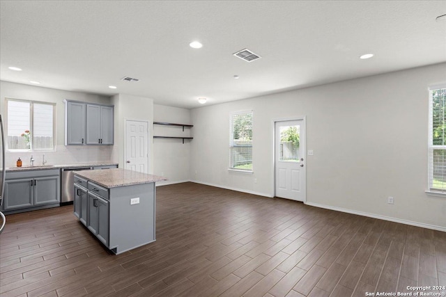 kitchen featuring gray cabinetry, dishwasher, a center island, decorative backsplash, and light stone counters