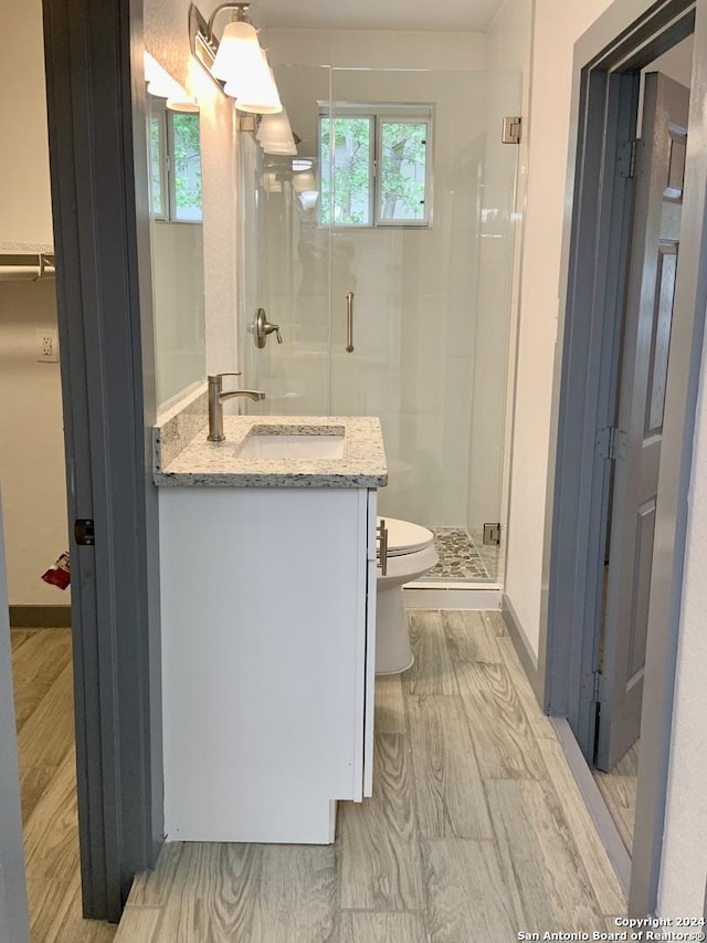 bathroom with toilet, a shower with shower door, wood-type flooring, and vanity