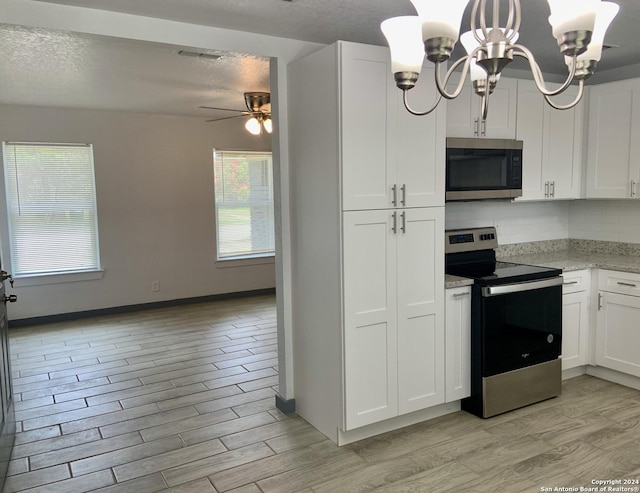 kitchen featuring appliances with stainless steel finishes, pendant lighting, white cabinets, light hardwood / wood-style flooring, and ceiling fan with notable chandelier