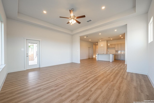 unfurnished living room featuring light wood finished floors, recessed lighting, ceiling fan, and a tray ceiling