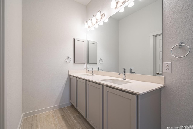 bathroom with wood tiled floor, double vanity, a sink, and baseboards