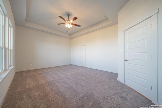unfurnished bedroom with carpet flooring, a tray ceiling, a ceiling fan, visible vents, and baseboards