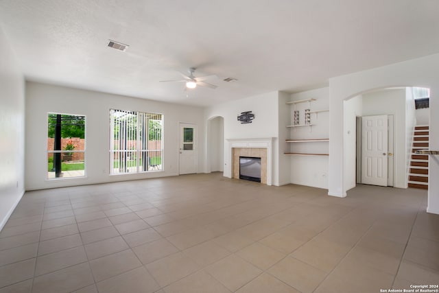 unfurnished living room with ceiling fan, a tile fireplace, and light tile floors