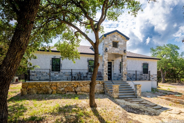 view of front of home featuring a shingled roof, stone siding, stairway, and stucco siding