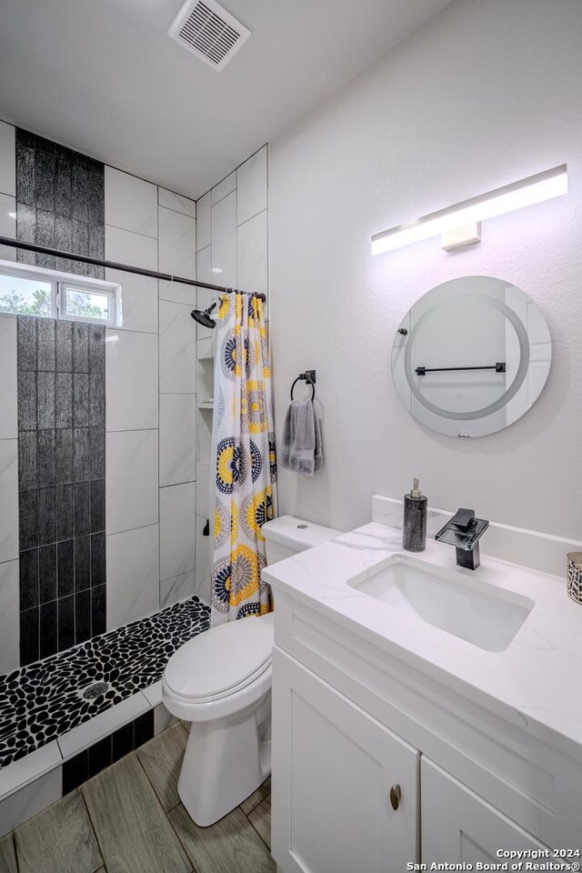 full bathroom with visible vents, tiled shower, toilet, vanity, and wood finish floors