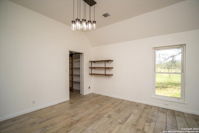 spare room with a notable chandelier, light wood-type flooring, and vaulted ceiling