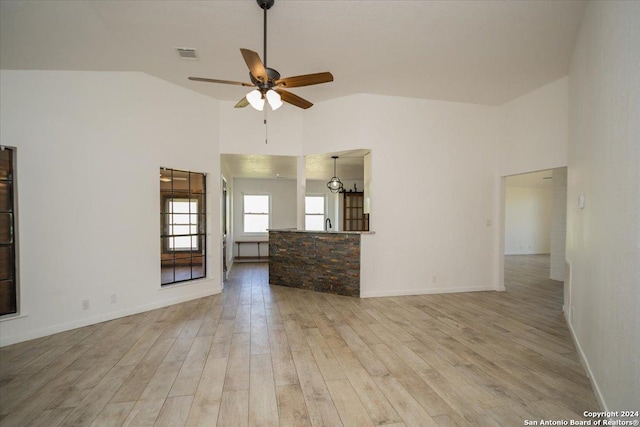 unfurnished living room featuring ceiling fan with notable chandelier, vaulted ceiling, and light hardwood / wood-style floors