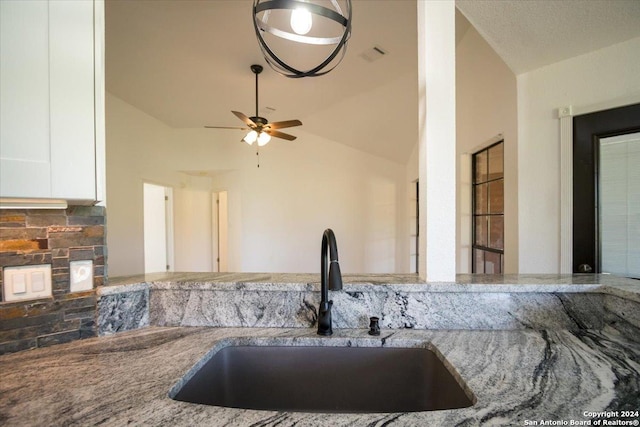 kitchen featuring white cabinets, vaulted ceiling, decorative backsplash, sink, and stone countertops