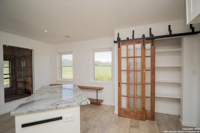 kitchen featuring a barn door, light hardwood / wood-style floors, light stone countertops, a textured ceiling, and white cabinetry