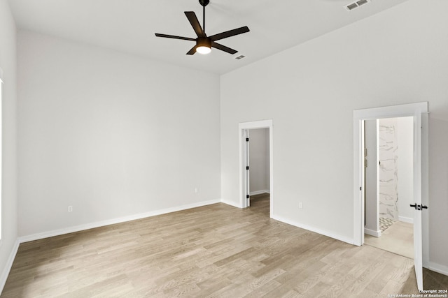 empty room featuring ceiling fan, a towering ceiling, and light hardwood / wood-style flooring