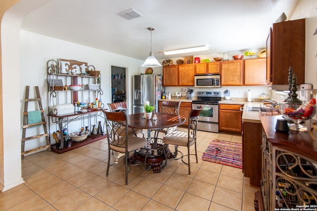 kitchen with appliances with stainless steel finishes, sink, hanging light fixtures, and light tile floors