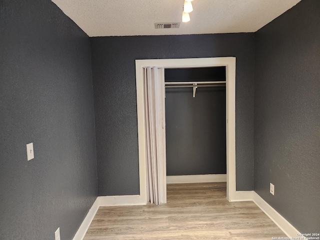 unfurnished bedroom with light hardwood / wood-style flooring, a textured ceiling, and a closet