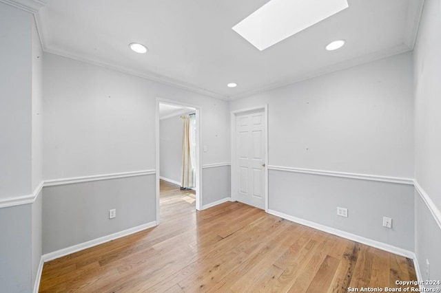 empty room featuring a skylight, crown molding, and light hardwood / wood-style floors