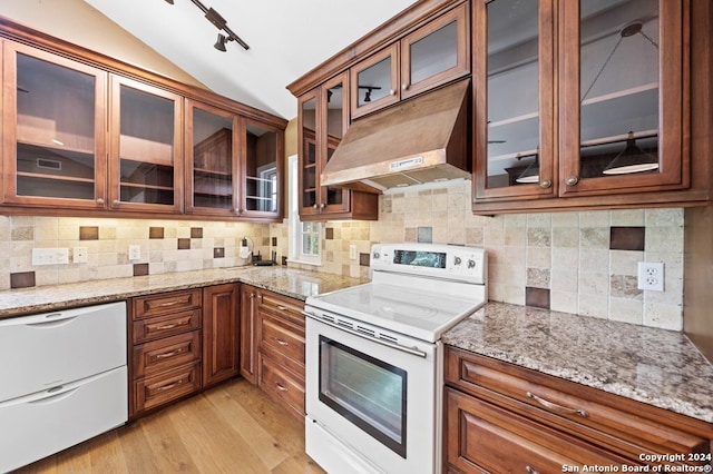 kitchen with tasteful backsplash, light stone counters, white appliances, vaulted ceiling, and light hardwood / wood-style flooring