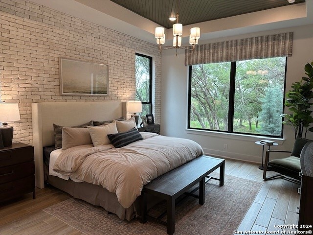 bedroom featuring brick wall, light hardwood / wood-style floors, a chandelier, and multiple windows