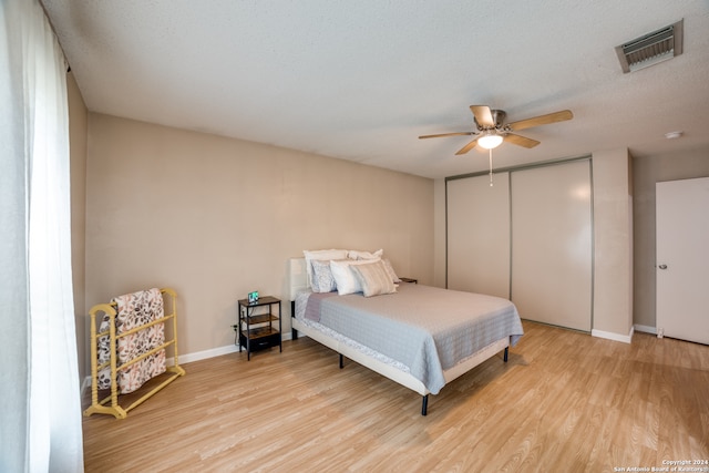 bedroom with a textured ceiling, light wood-type flooring, ceiling fan, and a closet