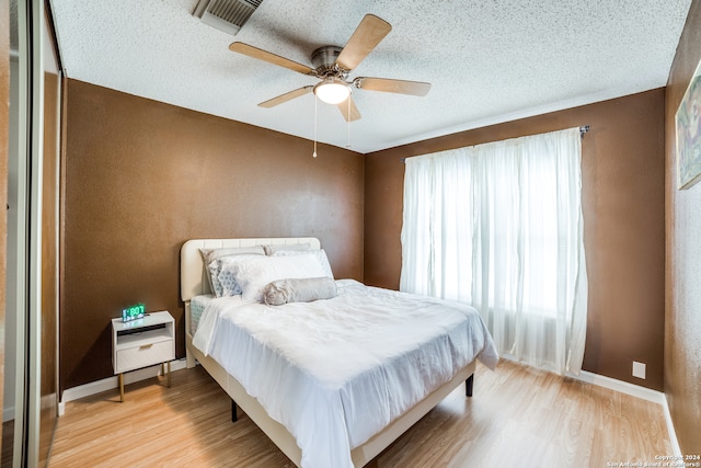 bedroom with light hardwood / wood-style flooring, multiple windows, a textured ceiling, and ceiling fan