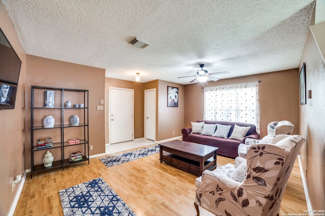 living room featuring light wood-type flooring, ceiling fan, and a textured ceiling