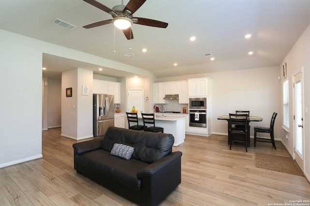 living room with ceiling fan, vaulted ceiling, and light wood-type flooring