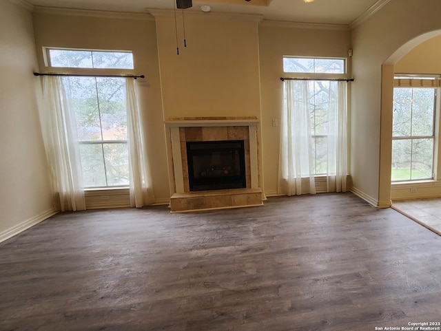 unfurnished living room featuring ornamental molding, a tile fireplace, hardwood / wood-style flooring, and a towering ceiling