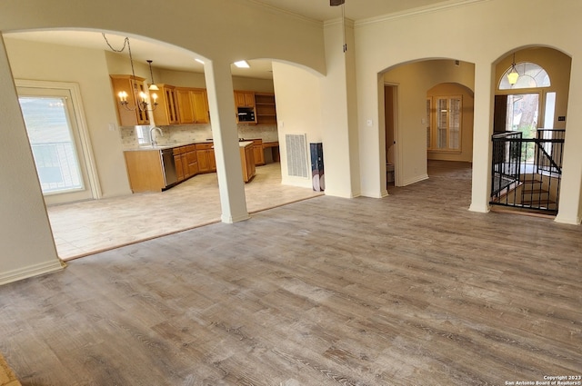 unfurnished living room featuring light hardwood / wood-style floors, a wealth of natural light, sink, and ornamental molding