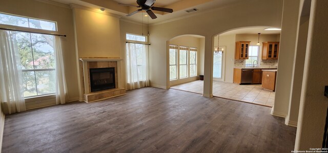 unfurnished living room featuring sink, a tiled fireplace, light wood-type flooring, ceiling fan, and ornamental molding