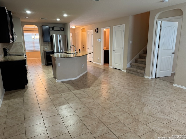 kitchen with a kitchen island with sink, sink, decorative backsplash, stainless steel fridge, and stone countertops