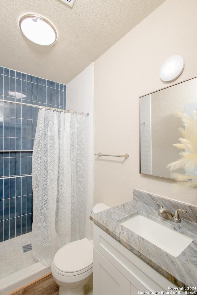 bathroom featuring a shower with shower curtain, vanity, toilet, and a textured ceiling