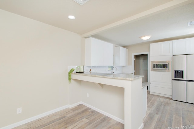 kitchen featuring stainless steel microwave, white fridge with ice dispenser, tasteful backsplash, kitchen peninsula, and white cabinets