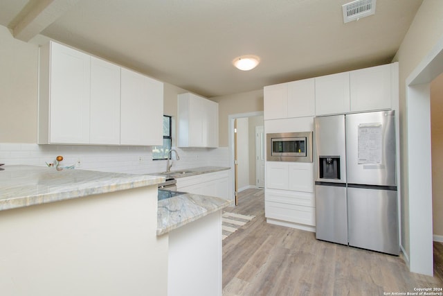 kitchen with white cabinets, appliances with stainless steel finishes, light stone countertops, and sink