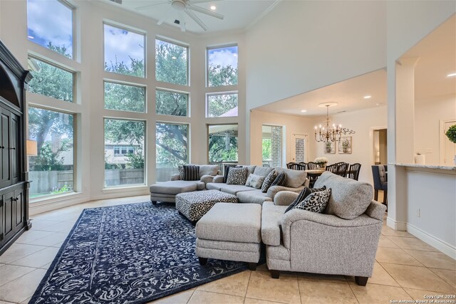 living room featuring light tile patterned flooring, ceiling fan with notable chandelier, ornamental molding, and a high ceiling