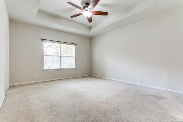 carpeted empty room featuring ceiling fan and a raised ceiling